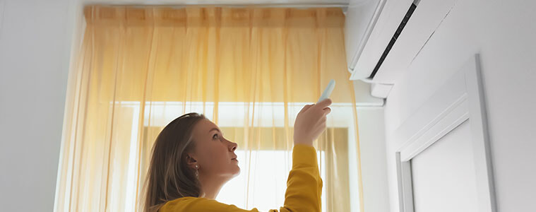 A woman aims a remote control at her wall-mounted air conditioner.