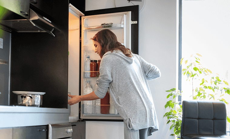 Woman opens a bottom mount fridge to remove ingredients for her lunch.