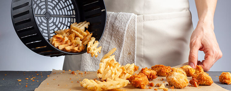 Someone serving air fryer waffle potato fries and fried chicken from an air fryer basket.