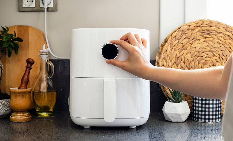 A hand adjusting a black dial on a white air fryer next to power point.
