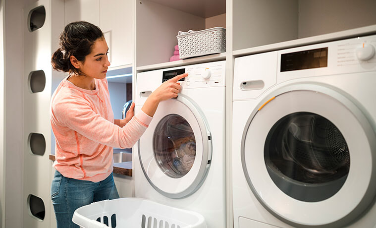 Young woman selects a program on a white washing machine in a home laundry. 