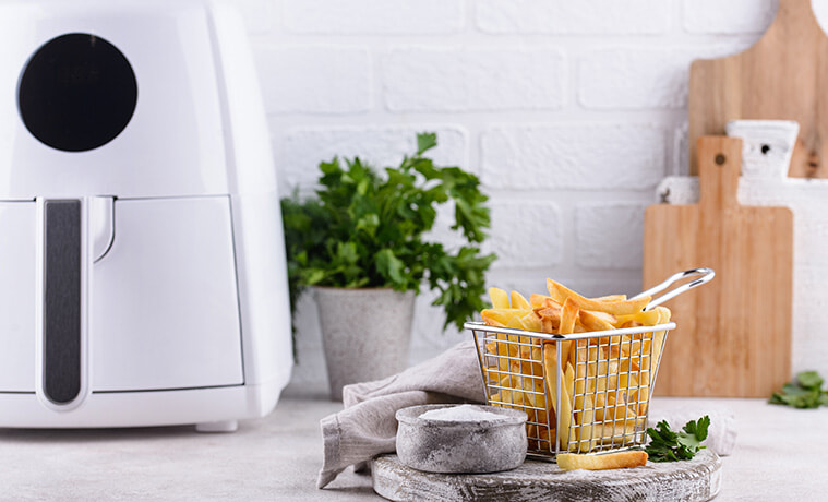 French fries near an air fryer on a kitchen bench.