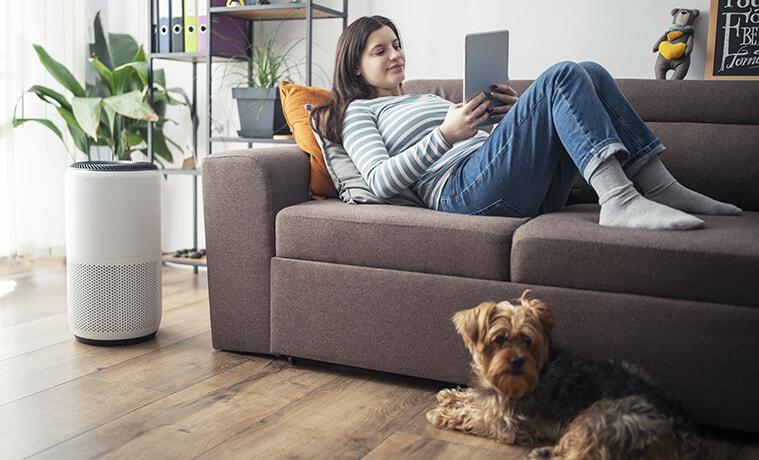 Young woman on a couch adjusts the setting of her home air purifier from her smart tablet