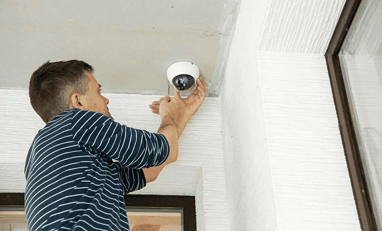 Man installing a security camera on the ceiling of his front porch, just near the front door.