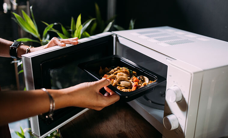 Close-up of a woman removing a frozen meal from a microwave oven.