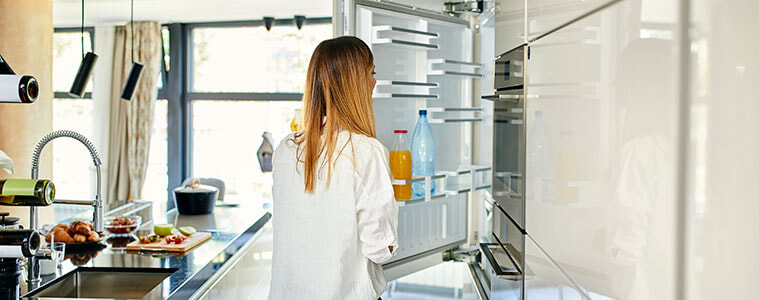 A woman opens the door of an integrated fridge in her modern and light-filled kitchen.