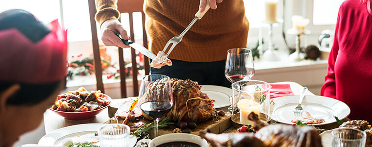 A family sits around the dining table on Christmas Day as the dad carves and serves the Christmas ham.