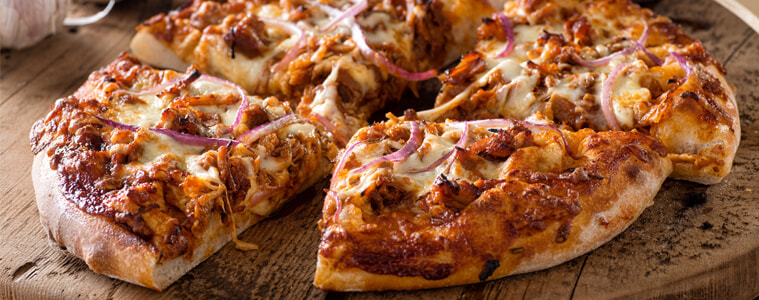 Spicy barbecue pulled pork pizza, sliced on a wooden board and ready to eat.