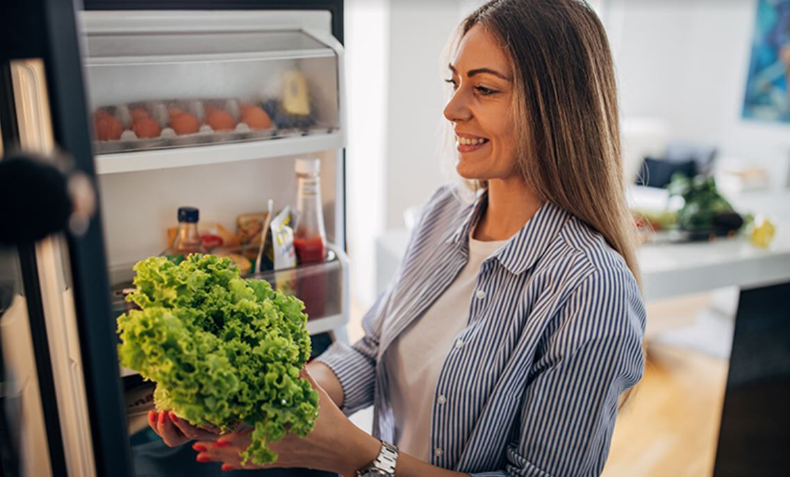 A woman removes a head of lettuce from her fridge.
