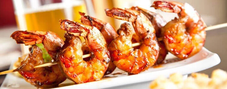Prawn skewers on a plate served with a drink.