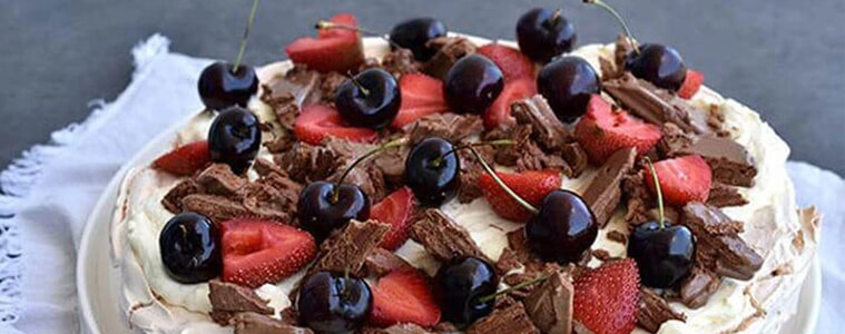 A pavlova topped with Tim Tams, cherries, and strawberries.