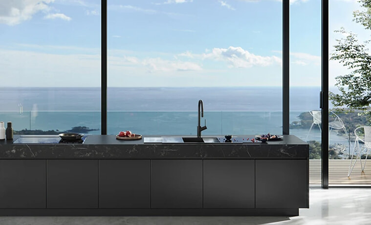 An all-black kitchen with a view of the ocean.