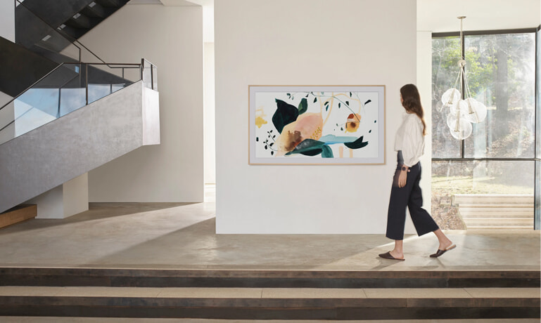 A woman walks past her TV disguised as artwork on the wall.