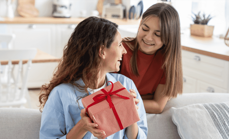 Mum receiving gift from daughter at home in the living room. 