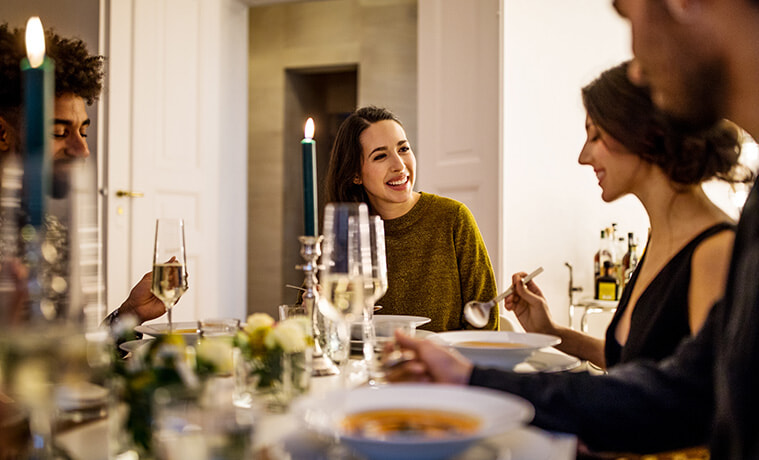 Smiling young woman talking with friends while having dinner at home.