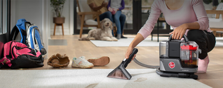 A woman cleans up muddy paw prints on her entryway rug while her dog watches.