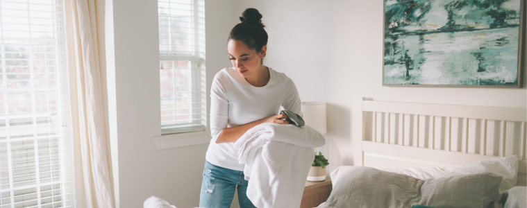 woman in a white bedroom cleaning her bed