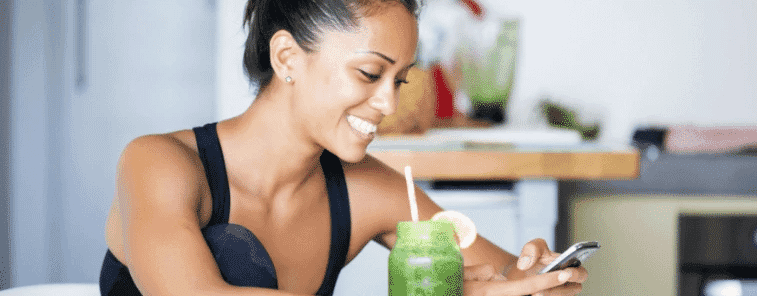 Woman smiles at phone next to a smoothie
