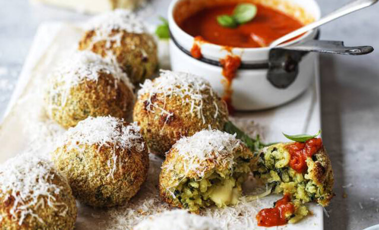 Spinach & mozzarella arancini with roast tomato sauce on a rectangular white plate.