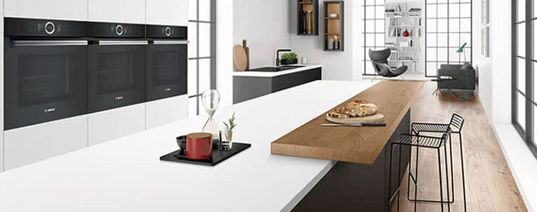 A black and white modern kitchen with 3 wall ovens.