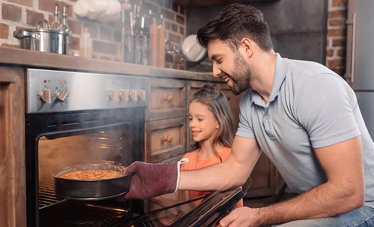Man pulls out cooking from his new steam oven whilst his daughter smiles and looks on
