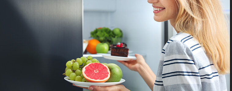 Woman taking plates with fruits and cake from a smart fridge in her kitchen. 