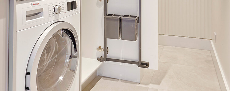 Detail of washing machine, dryer and tall cupboard with built-in internal storage racks attached to the inside of the cupboard door.