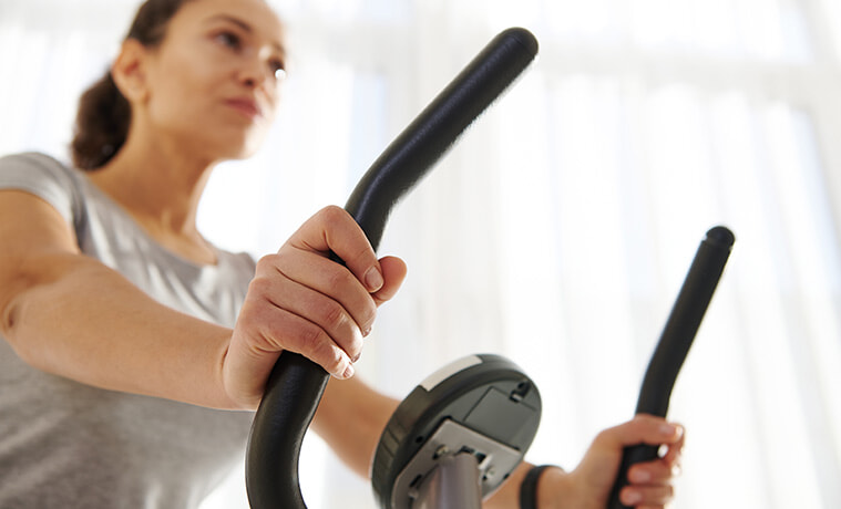 Close up view of hands of a woman riding an exercise bicycle during a cardio workout at home.