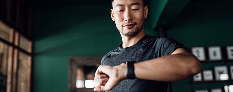Man exercising at home, using a fitness tracker app on his smartwatch to monitor training progress and measure his pulse. 