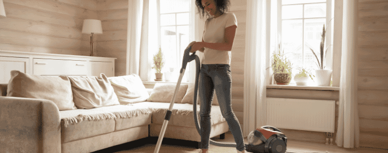 Woman cleaning her living room happily with her corded upright vacuum. 