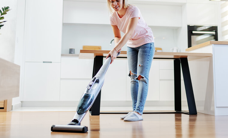 Woman using stick vacuum to clean her modern kitchen. 