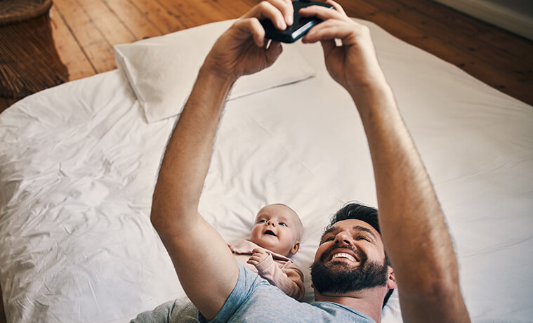 High angle shot of an affectionate young father taking selfies with his baby girl while lying on a bed at home.