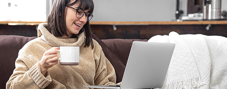 Woman sips coffee on the couch whilst practising mindfulness on her laptop. 