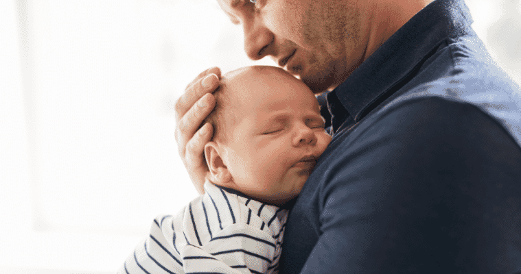 A new father is holding his newborn baby in a home nursery.