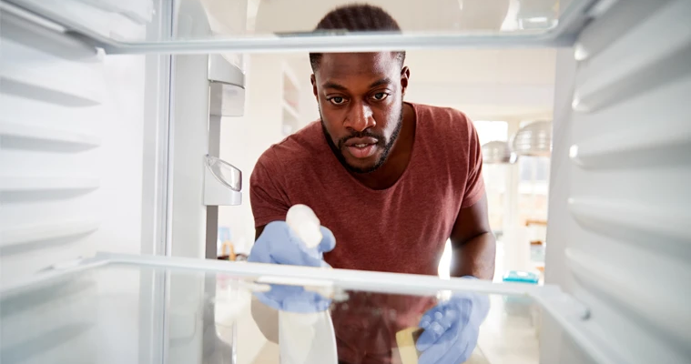 A man sprays and wipes down the interior of his fridge.