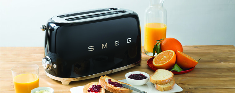 A black toaster surrounded by breakfast food on a light butchers block benchtop.