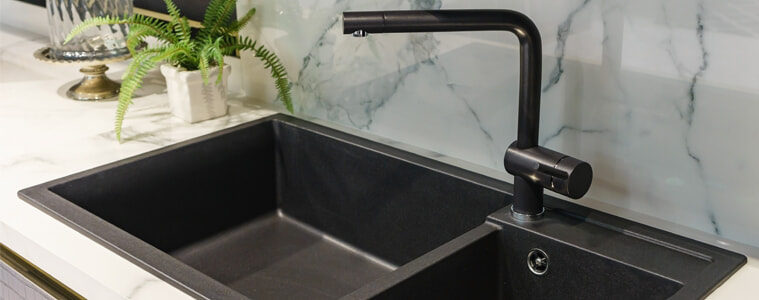A black sink and tap in a white kitchen.