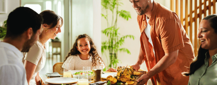 Family gathered at dinner table with man serving food