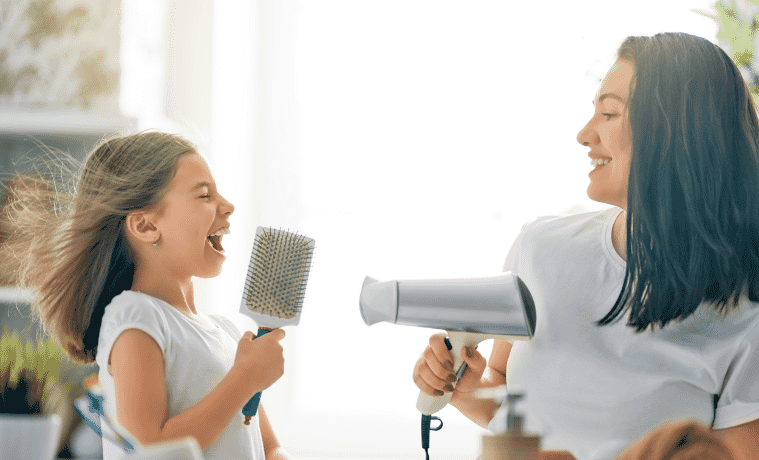 Mother and daughter laughing while using hairdryer