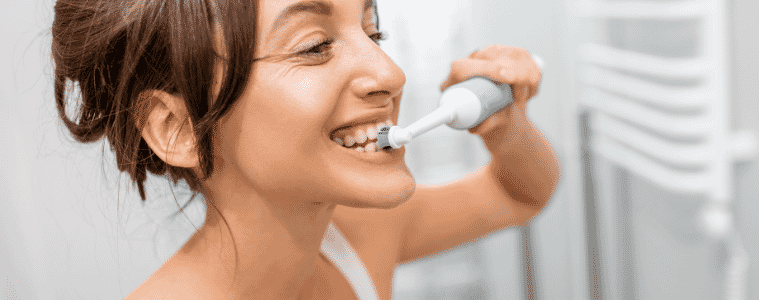 Young and cheerful woman brushing teeth with electric toothbrush