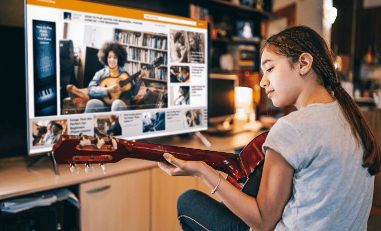 Girl playing guitar while taking an online music lesson on the smart TV in her living room
