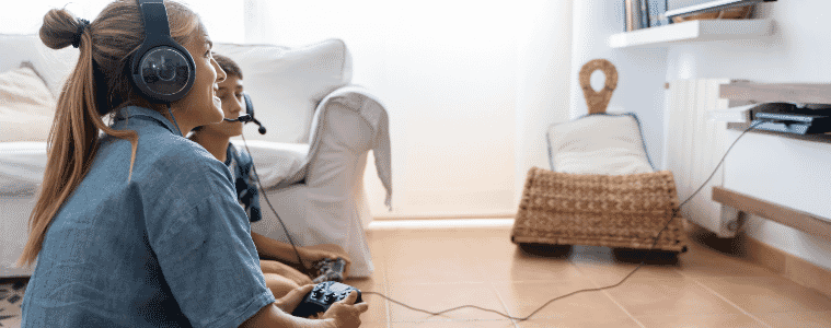 Teenagers sit on the floor and play video games on a console connected to the smart TV in their living room.