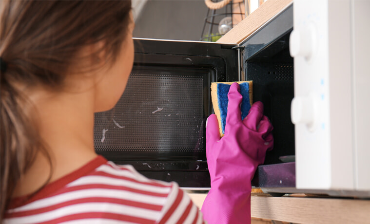 A woman cleans her microwave door.