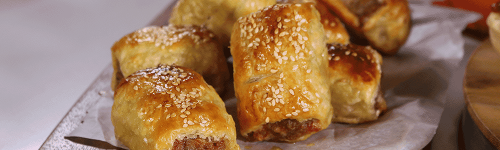 Golden sausage rolls stacked on a timber board. Image courtesy of Sunbeam