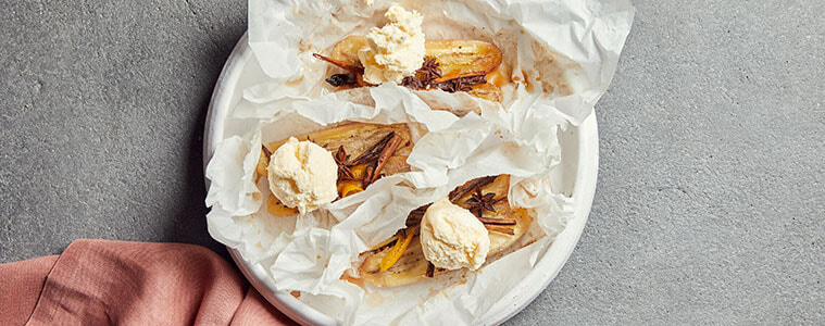 Bananas on crumpled greaseproof paper on a white plate with a grey background a salmon coloured napkin and a fork and spoon