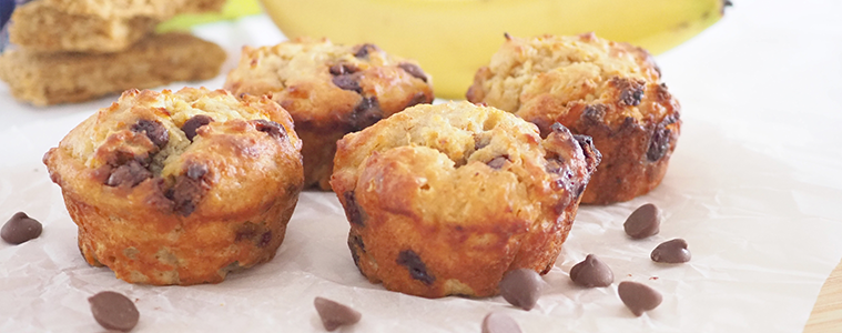 Banana and Weet-Bix Muffins on a white table with bananas and a scattering of chocolate chips