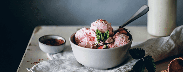 Scoops of delicious homemade strawberry ice cream in a white bowl on a white table with a white linen cloth.