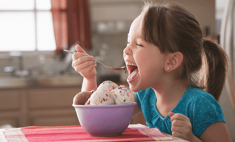 A cute little girl tucks into a bowl of ice cream and sprinkles in her kitchen