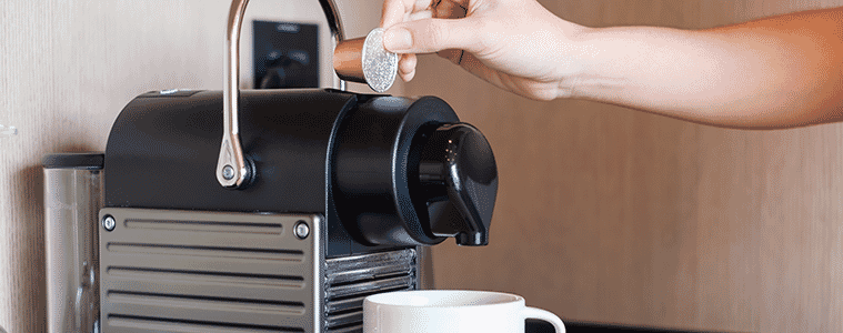 A woman places a coffee capsule into a capsule coffee machine