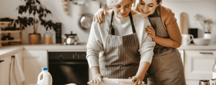 A woman stands behind an her mother as she bakes in a kitchen
